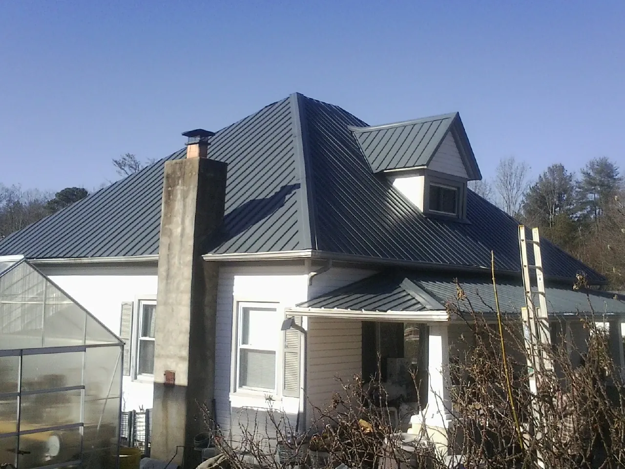 Dark blue standing seam metal roof on a white farmhouse with dormer — Slate & Tile Roof Repair by Roofing Brothers in Sargeant