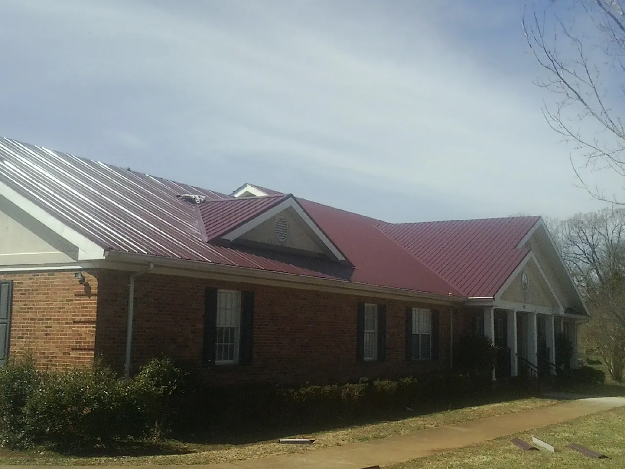 Red metal roof with gabled entries on a long brick building, from a Hail Damage Roof Repair job in Sargeant