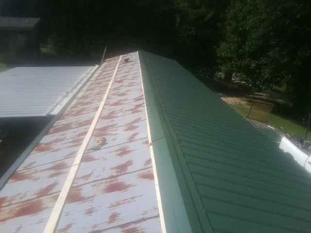 Old rusted panels beside newly installed green metal roofing — Wind Damage Roof Repair by Roofing Brothers in Sargeant