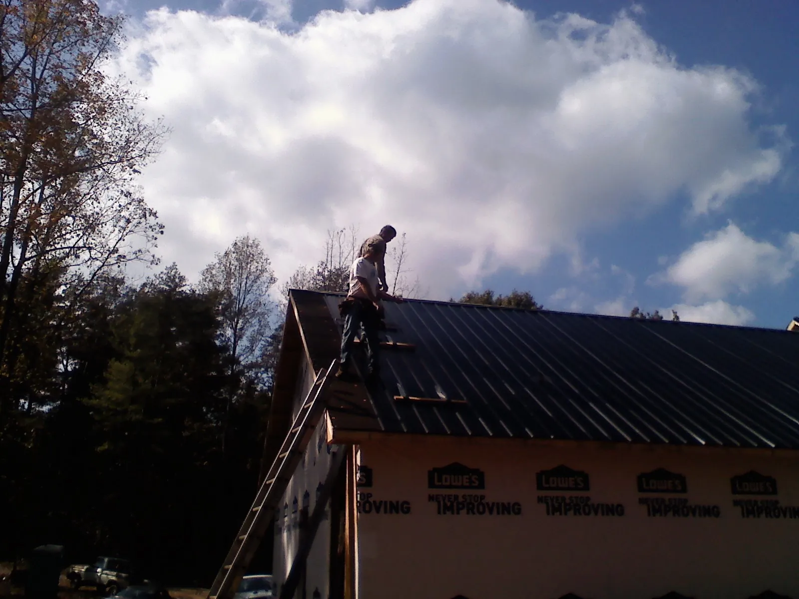 Roofer fastening dark metal panels high against a cloudy sky, from a Roof Inspection job in Sargeant