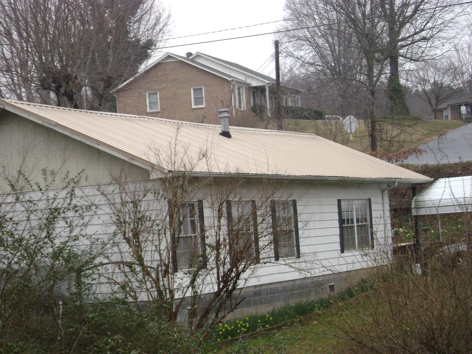 Tan metal roof on a white sided house set into a hillside — Commercial Roofing by Roofing Brothers in Sargeant